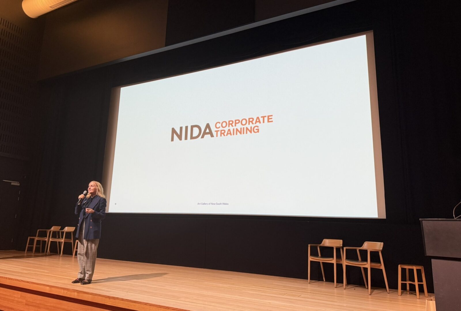 Presenter in front of a large screen with the NIDA Corporate Training logo